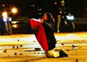 Albaneză, la protestele din Tirana, îngenunchiată în faţa poliţiştilor, oferindu-le drapelul ţării; în momentele următoare, un poliţist a ridicat-o, a sărutat drapelul şi a îmbrăţişat-o.
